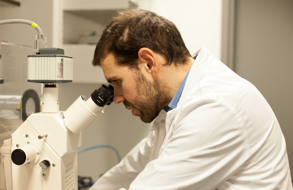 Man in white lab coat looking into microscope.